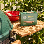 Big Green Egg grill with a box of Speedlight bulbs on a wooden surface outdoors.