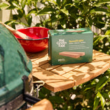 Big Green Egg grill with a box of Speedlight bulbs on a wooden surface outdoors.